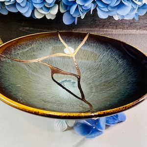 May include: A large, round, blue and brown ceramic bowl with a crackled glaze and gold accents. The bowl has a wide rim and a deep, rounded interior.