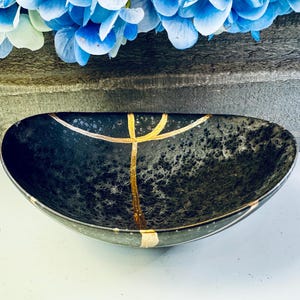 May include: A black ceramic bowl with gold accents. The bowl has a speckled finish and is oval shaped.