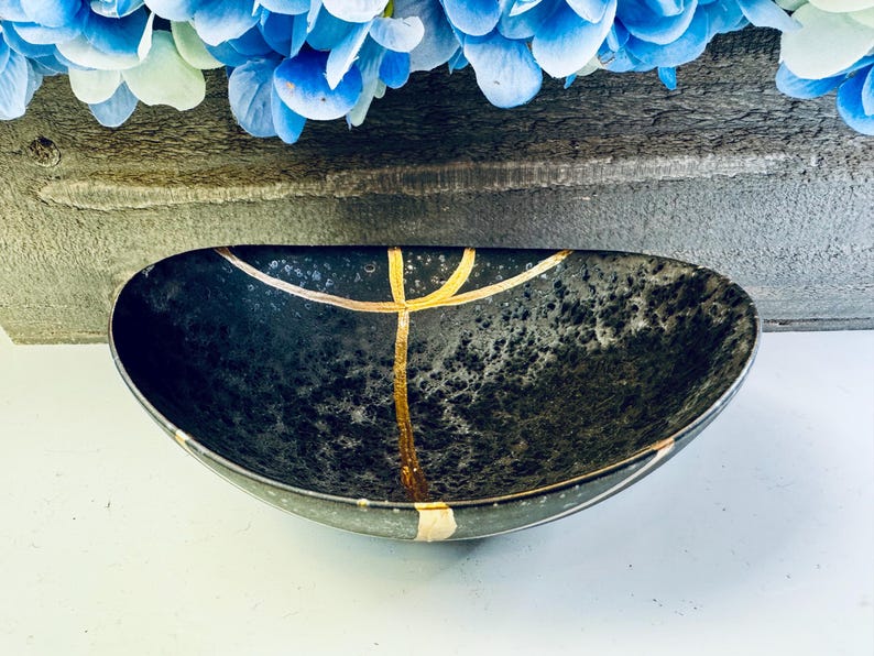 May include: A black ceramic bowl with gold accents. The bowl has a speckled finish and is oval shaped.