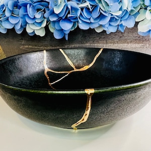 May include: A black ceramic bowl with gold crackle lines. The bowl has a distressed, aged look.