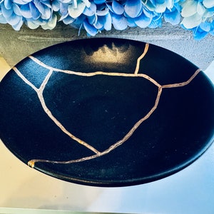 May include: A black ceramic bowl with a gold crackle design. The bowl is round and has a smooth, glossy finish.