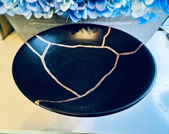May include: A black ceramic bowl with a gold crackle design. The bowl is round and has a smooth, glossy finish.