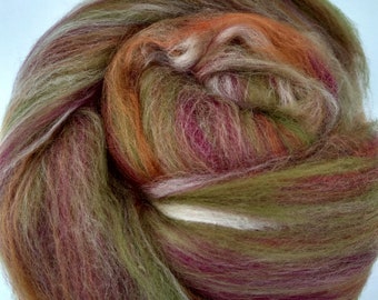 May include: A tightly wound bundle of colorful fiber, featuring a blend of olive green, burgundy, orange, and cream hues. The fibers have a soft, textured appearance, suggesting a natural material. This product is likely used for crafting, such as spinning or felting.