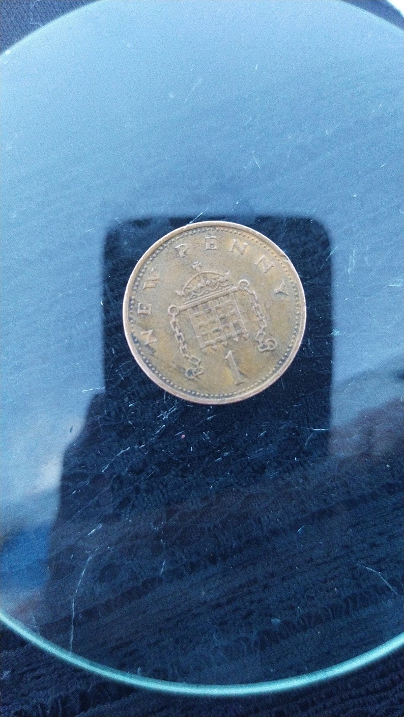 May include: A copper-colored British one penny coin with the inscription "ONE PENNY" and a depiction of the Royal Coat of Arms.