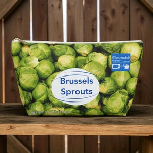 Könnte beinhalten: Eine Reißverschlusstasche mit einem lebendigen Aufdruck von grünen Rosenkohl. Die Tasche hat ein weißes ovales Etikett mit den Worten "Brussels Sprouts" in Blau. Das Nettogewicht beträgt 340g.