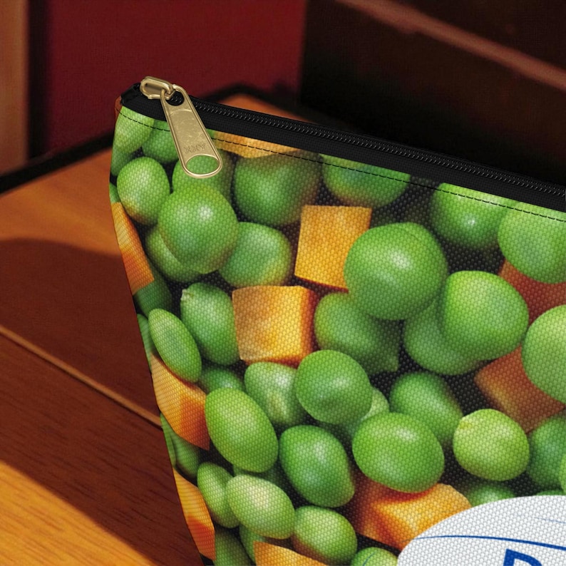 K&ouml;nnte beinhalten: Eine Kosmetiktasche mit Rei&szlig;verschluss und einem lebendigen Aufdruck aus gr&uuml;nen Erbsen und orangefarbenen, gew&uuml;rfelten Karotten. Die Tasche hat einen schwarzen Rei&szlig;verschluss und einen goldfarbenen Rei&szlig;verschlussanh&auml;nger. Das Design ist eine Nahaufnahme des Gem&uuml;ses und erzeugt ein frisches und farbenfrohes Muster.