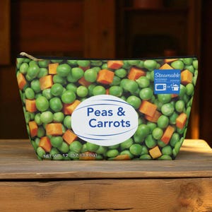 Può includere: Un beauty case con cerniera con un motivo di piselli verdi e cubetti di carote arancioni. La borsa ha un'etichetta ovale bianca con la scritta "Peas & Carrots". La borsa è etichettata "NET WT 340g" e "Steamable".