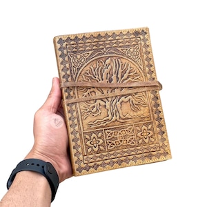 May include: A brown leather journal with a Celtic tree of life design and a brown leather strap closure.