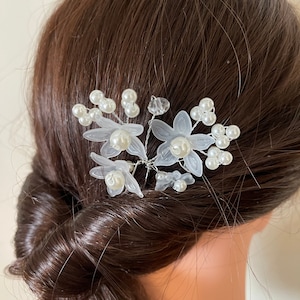 May include: White floral hair comb with pearl accents. The comb is made of plastic and wire and features delicate white flowers and pearls.