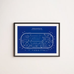 May include: Framed blueprint-style print of the Indianapolis Motor Speedway. The print features a detailed white outline of the track layout against a blue background, with labeled sections and the text "Indianapolis". The print is in a black frame.