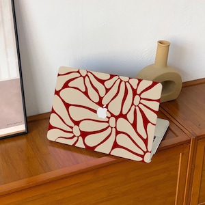 Könnte beinhalten: Ein Laptop mit einem cremefarbenen Gehäuse und einem roten Blumendesign. Der Laptop steht auf einer Holzoberfläche.