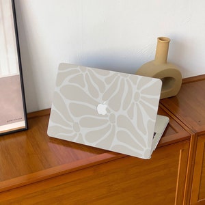 May include: A light grey laptop computer with a white abstract floral pattern on the lid. The laptop is sitting on a wooden surface.