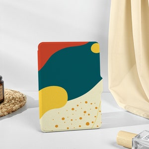 Könnte beinhalten: Eine E-Reader-Hülle mit einem bunten, abstrakten Design. Das Design zeigt ein abstraktes Muster in Tealblau, Gelb und Rot.