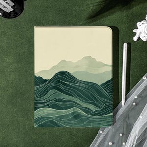 Peut inclure: Une couverture de carnet de couleur crème avec un motif de paysage de montagne vert et blanc. La couverture a une texture subtile et une finition mate.