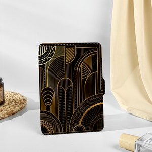 Op de afbeelding: Een e-reader hoes met een geometrisch patroon in zwart en goud, in Art Deco-stijl.