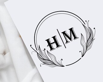 Könnte beinhalten: Ein schwarz-weißes Monogramm-Design mit den Initialen "H/M" in einem Kreis mit floralen Akzenten.
