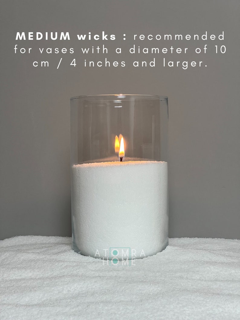 May include: A white candle burning in a clear glass jar. The candle is sitting on a white surface. The text "MEDIUM wicks: recommended for vases with a diameter of 10 cm / 4 inches and larger." is displayed above the candle.