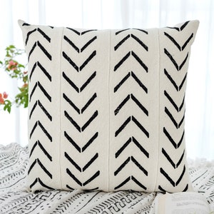 Könnte beinhalten: Ein weißes Kissen mit einem schwarzen Chevron-Muster. Das Kissen ist aus einem weichen, strukturierten Stoff gefertigt und hat ein schlichtes, modernes Design.