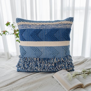 May include: Blue and white woven throw pillow with a fringe border. The pillow has a geometric pattern and is made of a soft, textured fabric.