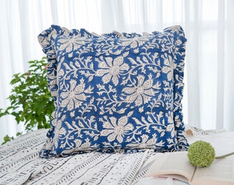 May include: A blue and white floral patterned pillow with a ruffled edge. The pillow is lying on a white and black patterned blanket.