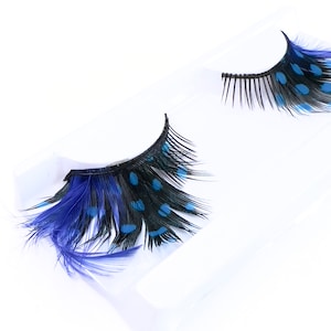 May include: A pair of false eyelashes with blue and black feathers. The feathers have a polka dot pattern.