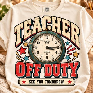 May include: A cream-colored t-shirt featuring a graphic of a vintage-style clock with the text TEACHER OFF DUTY. The clock face reads SCHOOL TIME and ALWAYS A GOOD IDEA with a heart symbol. Red and blue stars surround the clock, and the bottom text reads SEE YOU TOMORROW.