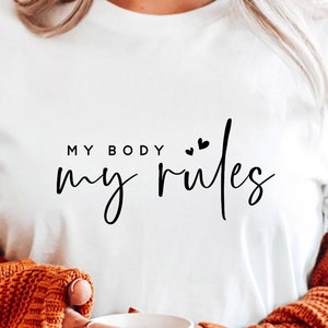 Puede incluir: Camiseta blanca con el texto "MY BODY my rules" en letra cursiva negra con dos pequeños corazones sobre la palabra "rules".