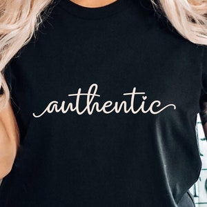 Op de afbeelding: Een zwart T-shirt met het woord "authentiek" in witte cursieve letters.