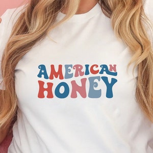 May include: White t-shirt with the text "AMERICAN HONEY" in red, white, and blue retro font.