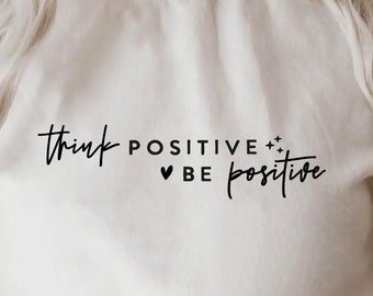 Peut inclure: Sweat-shirt blanc avec le texte "Think Positive + Be Positive" en lettres noires.