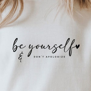 Puede incluir: Sudadera blanca con el texto "be yourself & don't apologize" en letras negras con un pequeño símbolo de corazón.