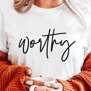 May include: White t-shirt with the word "worthy" written in black cursive script.