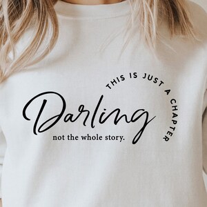 May include: White sweatshirt with black text that reads "This is just a chapter, Darling, not the whole story."