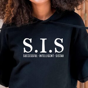 Può includere: Felpa con cappuccio nera corta con una grafica bianca che dice "S.I.S. Successful - Intelligent - Sistah"