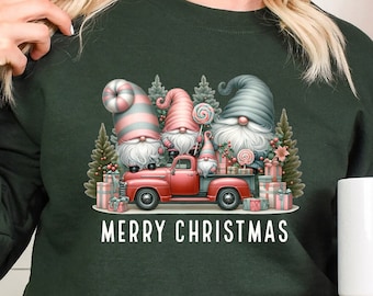 May include: Green Christmas sweatshirt with a red truck carrying three gnomes and presents. The gnomes are wearing hats and holding candy canes. The text "Merry Christmas" is printed below the truck.