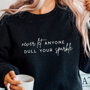 Op de afbeelding: Zwart sweatshirt met witte tekst die "never let anyone dull your sparkle" zegt.