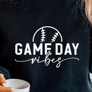以下が含まれることがあります： 白い野球のグラフィックと「GAME DAY vibes」というテキストが書かれた黒いスウェットシャツ。