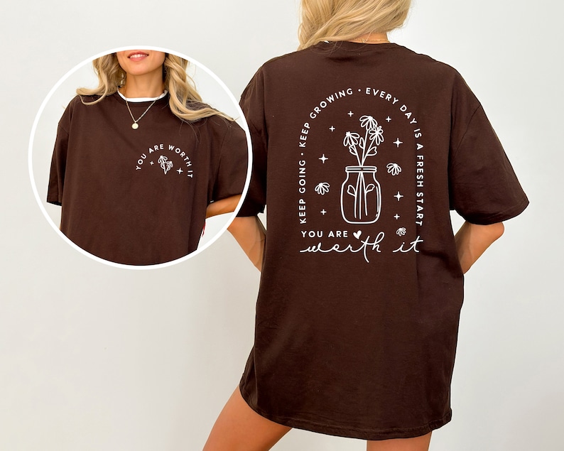 May include: Brown oversized t-shirt with a white graphic print on the back that says "Keep going. Keep growing. Every day is a fresh start. You are worth it." The graphic features a jar with flowers and stars.