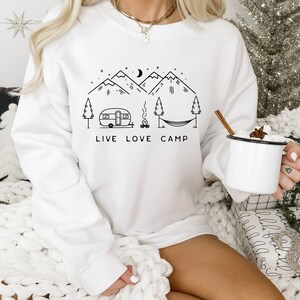 May include: White sweatshirt with a black graphic design of mountains, a camper, a campfire, a hammock, and the text "Live Love Camp".