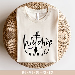 May include: A white t-shirt with a black graphic design that says "Witchy Mama" with a witch's hat, broom, and stars.