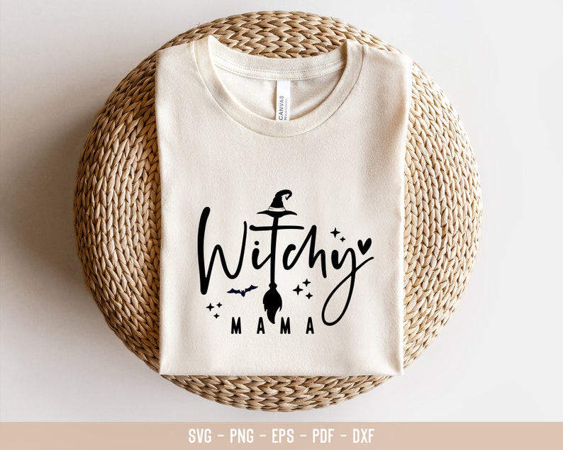 May include: A white t-shirt with a black graphic design that says "Witchy Mama" with a witch's hat, broom, and stars.