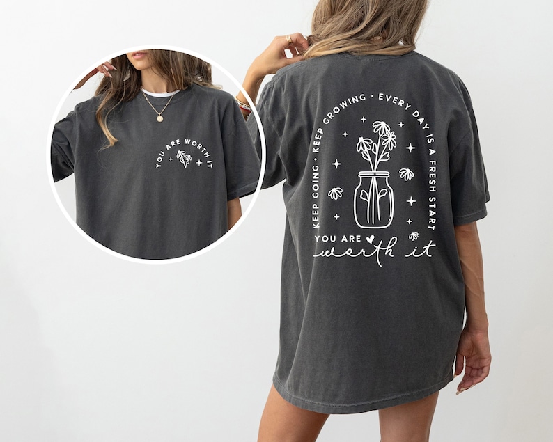 May include: A dark gray t-shirt with a white graphic on the front that says "You are worth it" and a white graphic on the back that says "Keep growing. Every day is a fresh start. You are worth it." The graphic on the back features a jar with flowers.
