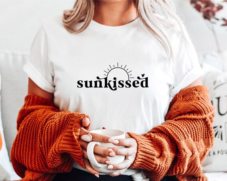 May include: White t-shirt with a black graphic of a sun with rays and the word "sunkissed" in a retro font.