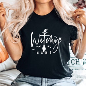 May include: Black t-shirt with a white graphic that says "Witchy Mama" with a witch's hat, broom, and stars.