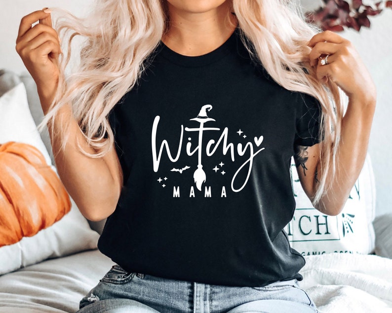 May include: Black t-shirt with a white graphic that says "Witchy Mama" with a witch's hat, broom, and stars.