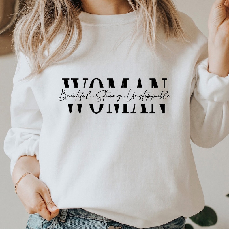 May include: White sweatshirt with black text that reads "WOMAN Beautiful. Strong. Unstoppable WOMAN".