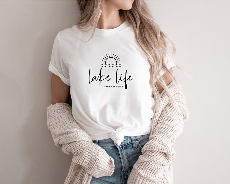 Peut inclure: T-shirt blanc avec un graphique noir d'un soleil couchant sur l'eau et le texte "lake life is the best life".