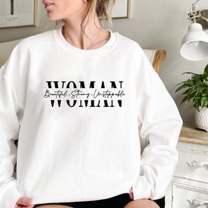 May include: White sweatshirt with black text that reads "WOMAN Beautiful. Strong. Unstoppable WOMAN".