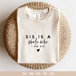 May include: A white t-shirt with black text that reads "SIS IS A whole vibe I AM SIS" with a small black heart below the text.