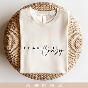 May include: A white t-shirt with the text "BEAUTIFUL crazy" printed on it. The shirt is folded and placed on a woven straw mat.